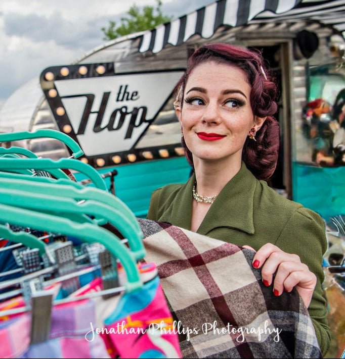 Woman holding a plaid skirt with 'The Hop' sign in the background